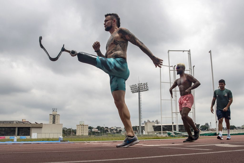 Imagem da pista de atletismo do centro paralímpico, um local aberto, em que aparecem dois atletas com deficiência para o treino de corrida.