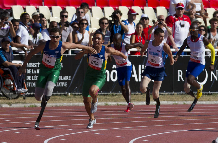 Cinco atletas paraolimpicos correm em uma pista de corrida