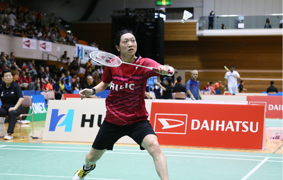 Foto de Ayako jogando uma partida. Tem cabelo preto e está vestida com uma camisa vinho e short preto.