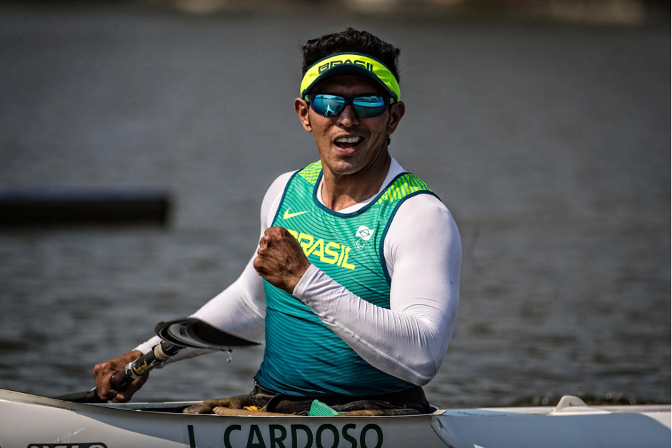 Atleta Luis Carlos Cardoso, homem pardo, usando uma blusa tipo segunda pele branca, com uma camiseta verde por cima, óculos escuros e um boné verde. Ele está sentado na canoa e segurando o remo com a mão direita (Foto: CPB)