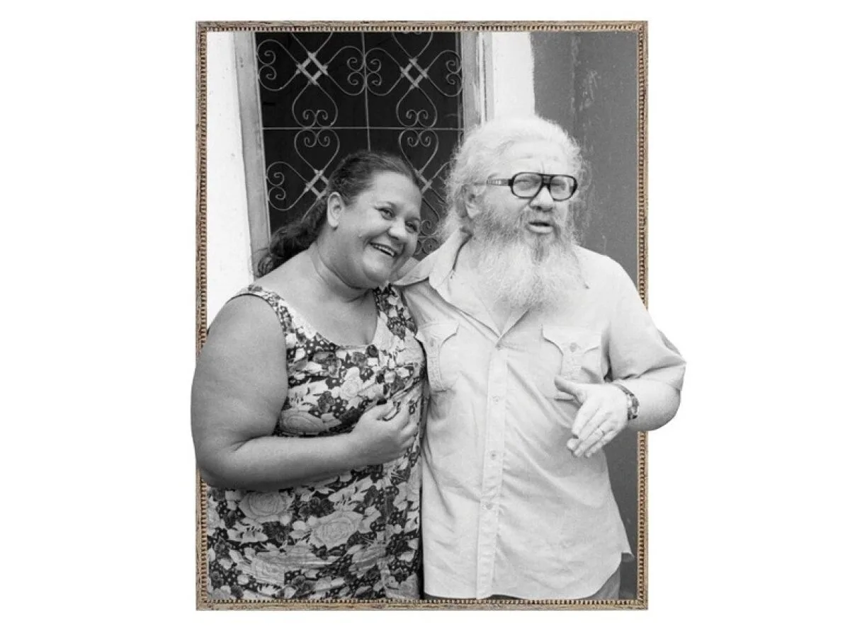 Imagem de um casal abraçado em frente a um portão.