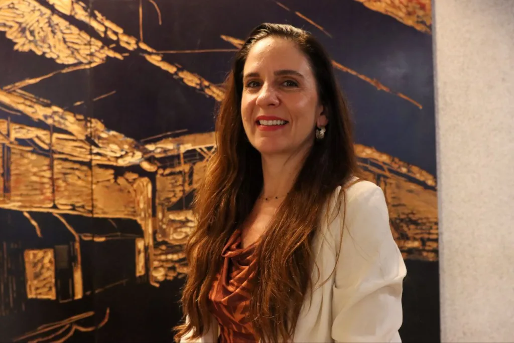 Mariana Meirelles sorri em frente a um quadro dourado